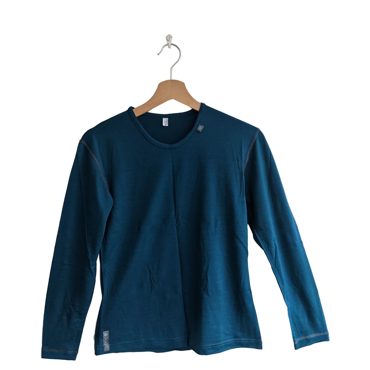 A dark teal long-sleeve merino wool crewneck shirt hanging on a wooden hanger against a plain light gray wall.