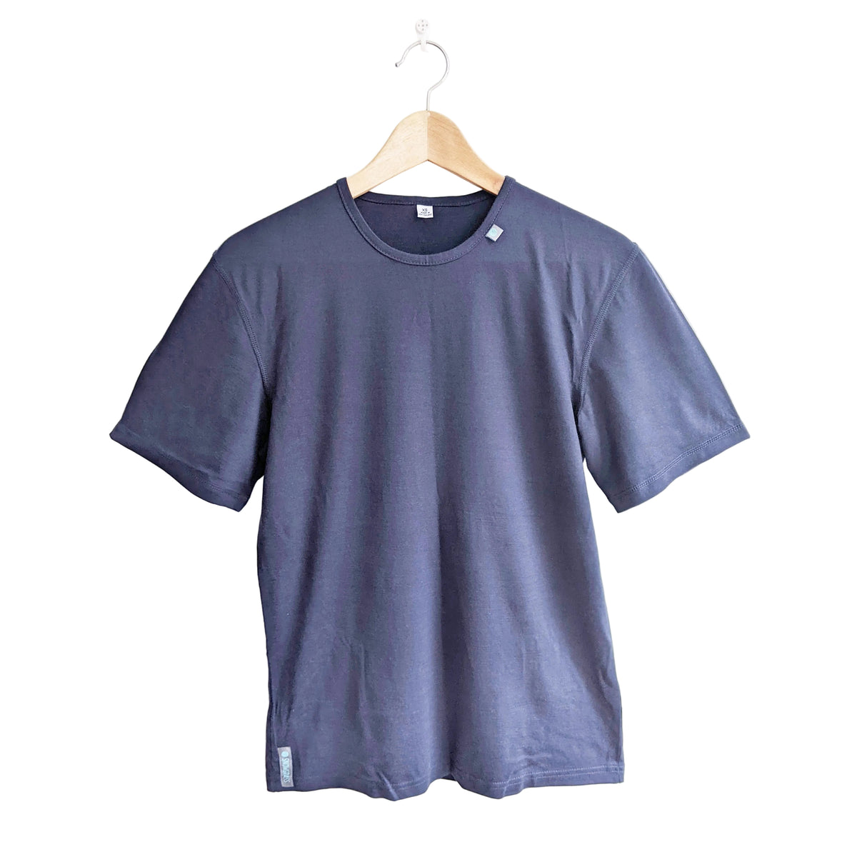 A dark blue crewneck merino wool short-sleeve t-shirt hanging on a wooden hanger against a plain white wall.