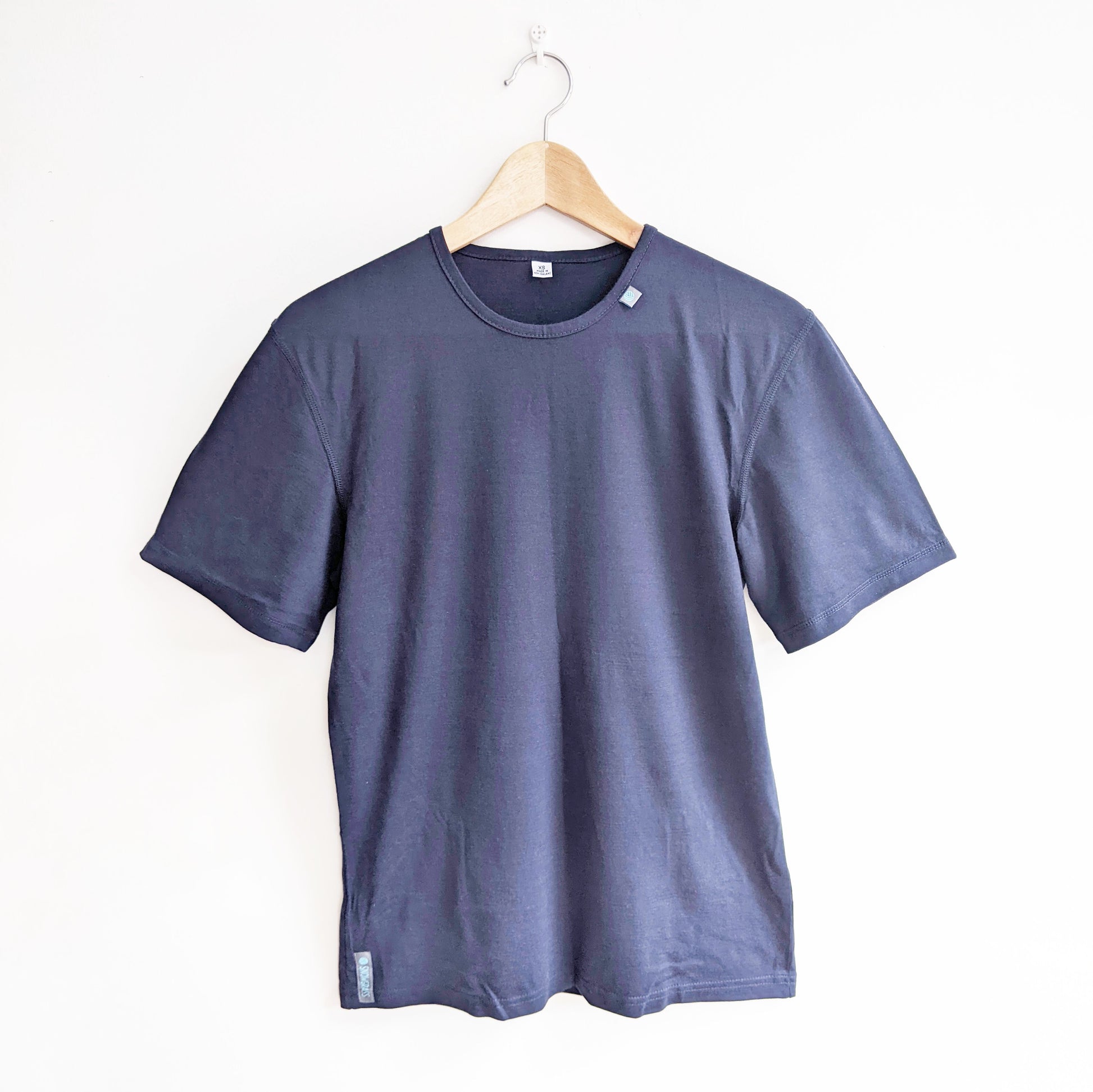 A dark blue crewneck merino wool short-sleeve t-shirt hanging on a wooden hanger against a plain white wall.